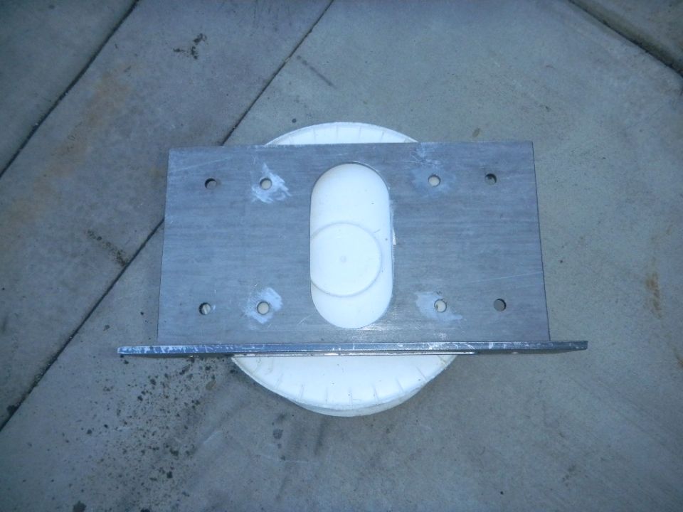 metal bracket with white plastic insert, sitting on a white circular object on concrete