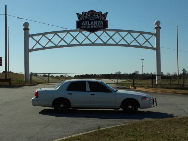 Silver Ford sedan with black wheels and push bar parked under Atlanta Motor Speedway arch