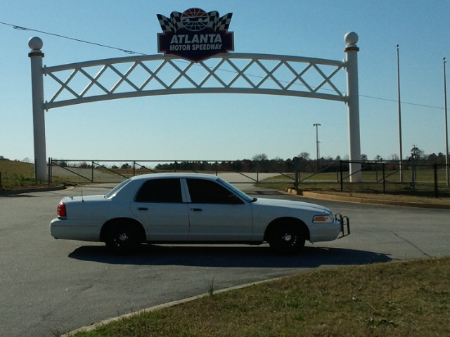 White Crown Victoria with push bar and black wheels parked under Atlanta Motor Speedway entrance arch