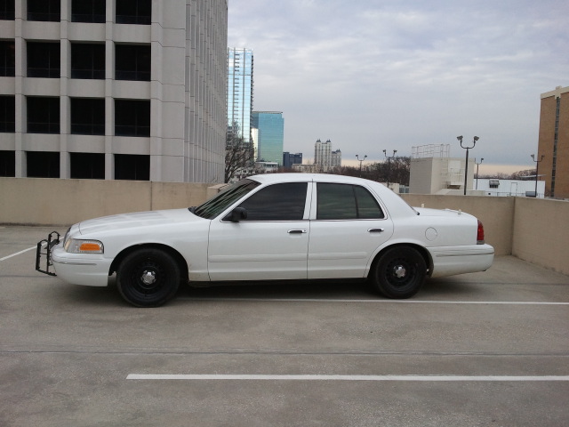 White Crown Victoria sedan side profile on rooftop parking deck with push bumper and black steel wheels