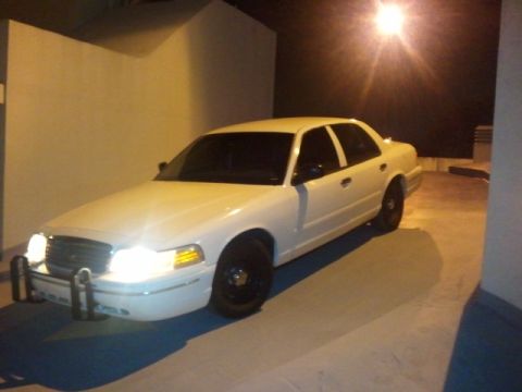 1998 Ford Crown Victoria - A white 1998 Ford Crown Victoria is parked under artificial lighting, showing its front and side profile.