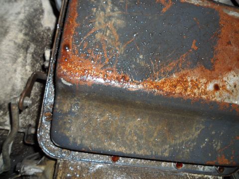 1989 Ford Bronco - Close-up of a heavily rusted and oil-stained oil pan, showing its gasket and mounting bolts.