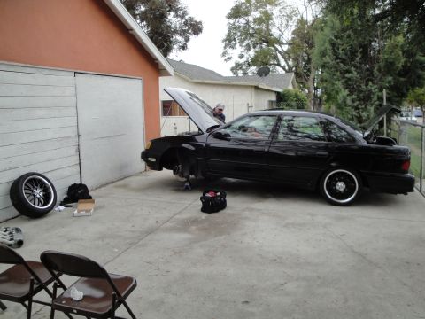 2003 Ford Taurus - A black sedan is parked outside a garage with its hood and trunk open, undergoing maintenance.
