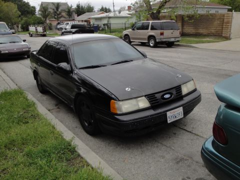 2003 Ford Taurus - This black sedan, possibly a first-generation Ford Taurus, is parked on a residential street.