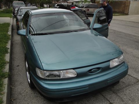 2003 Ford Taurus - A teal sedan is parked on the street with its doors open, and a man is standing next to it.