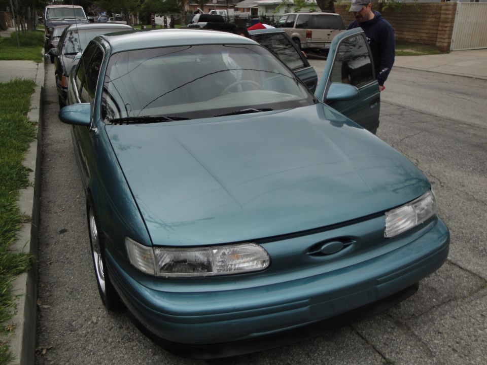 Teal sedan with doors open, parked on a residential street. A man stands by the driver's door