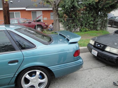 2003 Ford Taurus - A teal sedan with a spoiler and custom wheels is parked next to a dark sedan.