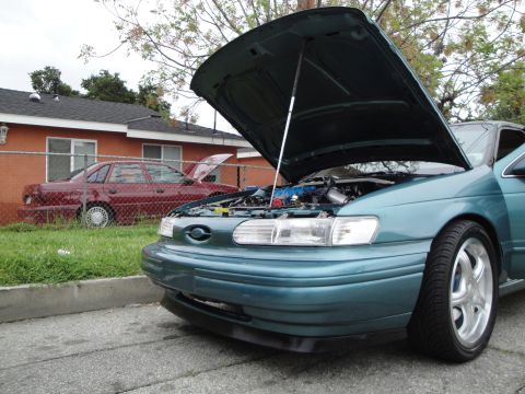 2003 Ford Taurus - Two sedans parked on a street, both with hoods open. One is teal, the other is red.