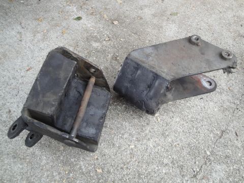 2003 Ford Taurus - Two worn engine mounts, one with a metal bracket attached, lie on a concrete surface.