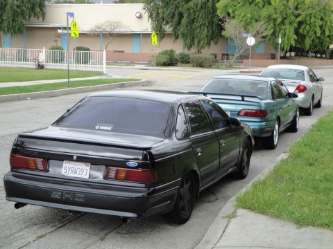 2003 Ford Taurus - A black Ford Taurus SHO is parked on the street, with two other vehicles behind it.