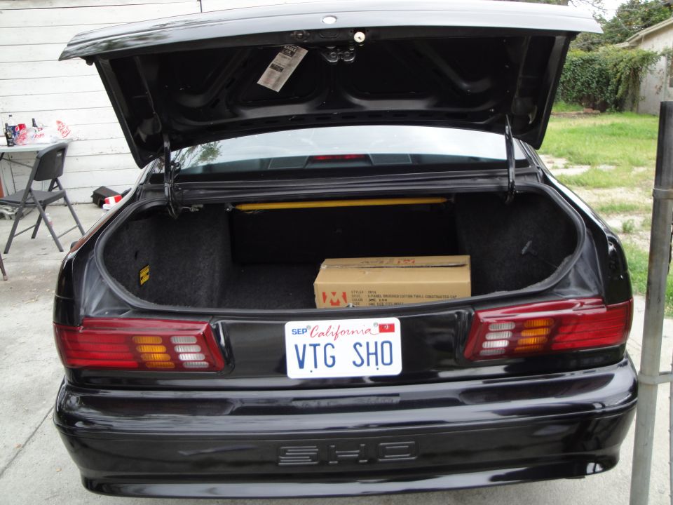 Black sedan's open trunk with a cardboard box inside and a California license plate reading VTG SHO