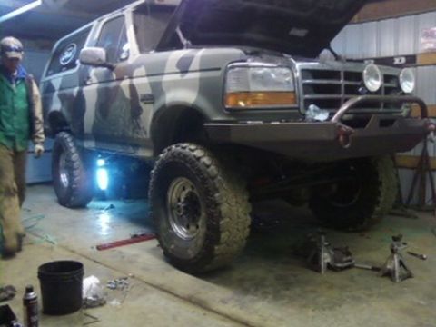 1995 Ford Bronco - A camouflaged Ford Bronco is parked in a garage with its hood open and aftermarket modifications.
