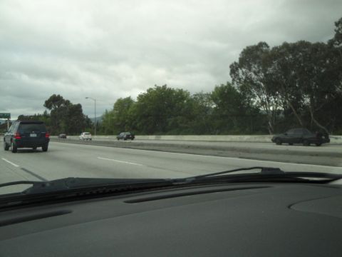 2003 Ford Taurus - Multiple vehicles travel along a highway under an overcast sky, with trees lining the roadside.