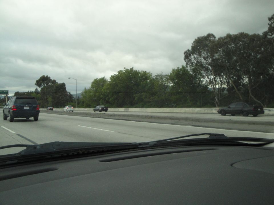 Cars driving on a cloudy day on a highway with trees and a concrete barrier