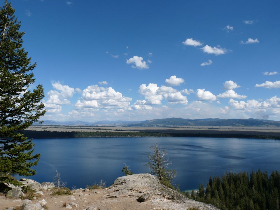 Scenic lake and mountain landscape with trees in the foreground and a blue sky with clouds