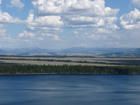 2006 Ford E350 - A vast landscape a calm blue lake in the foreground, with rolling hills and mountains in the distance under a sky filled with white clouds.