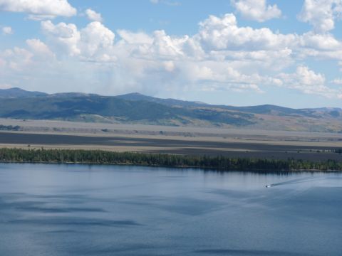 2006 Ford E350 - A lone boat travels across a vast blue lake, with a dense forest and distant mountains under a partly cloudy sky.