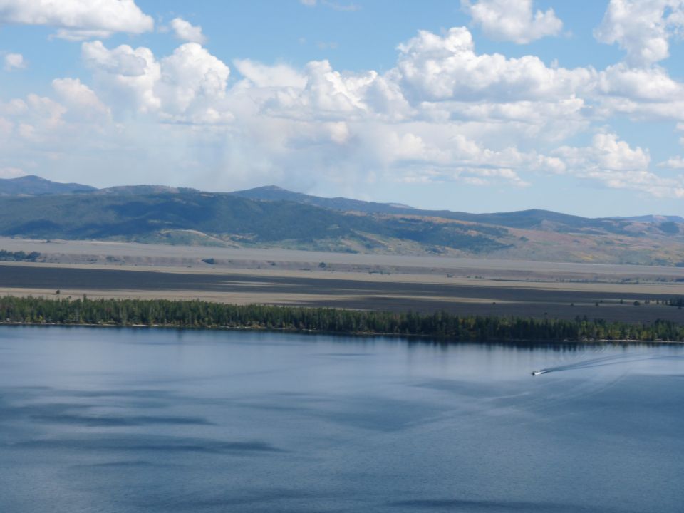 Boat on a blue lake with a tree line and mountains under a cloudy sky