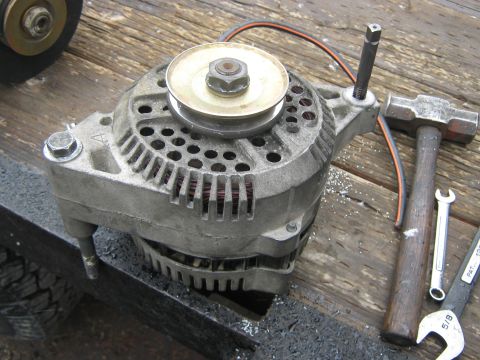 1972 Ford F-250 - An alternator sits on a wooden surface next to a hammer and wrench, suggesting a repair or rebuild process.