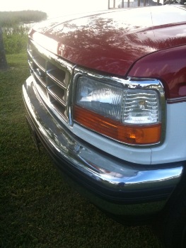 1995 Ford Bronco - Close-up of the front end of a red and white truck, showing the grille and headlights.