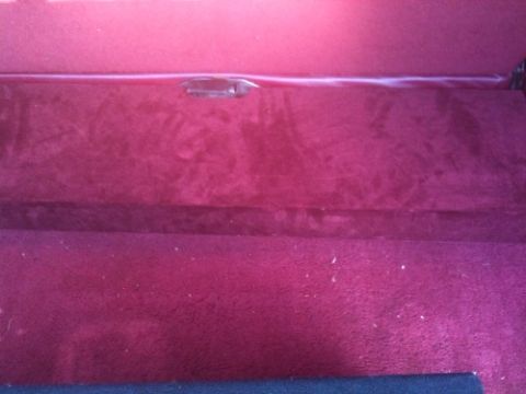 1995 Ford Bronco - The interior of a vehicle shows red carpeting and a dark trim piece with a handle.