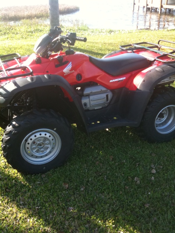 Red Honda Rancher ATV four-wheeler parked on grass by water