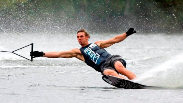 Guy waterskiing, holding tow rope. Water spraying up