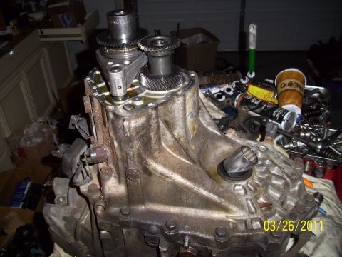 1995 Ford Probe - Close-up of a transmission assembly, showing gears and housing, with various tools and a coffee cup nearby.