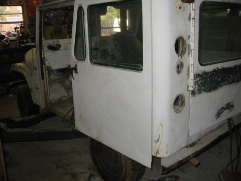 1974 Jeep CJ5 - A white van body, possibly undergoing restoration, is shown with its driver's door ajar, revealing the interior and front wheel area.
