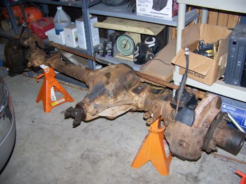 1992 Jeep YJ - Front axle assembly, likely from a Jeep, is shown disassembled and supported by orange jack stands in a garage setting.