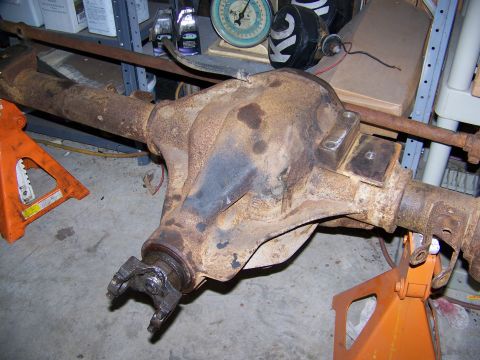 1992 Jeep YJ - A rusty rear axle assembly is supported by orange jack stands in a garage setting.