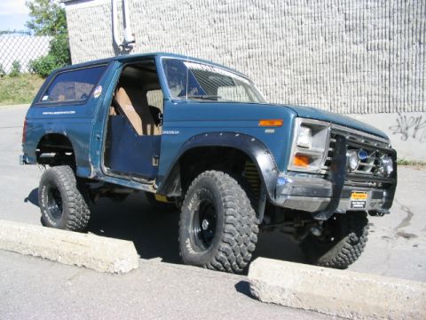 1986 Ford Bronco - Modified blue Ford Bronco with off-road tires and suspension lift.