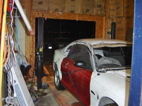 1984 Ford Mustang - A damaged car sits in a garage, with another vehicle visible in the background.