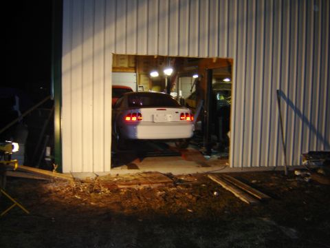 1984 Ford Mustang - A white Ford Mustang is seen on a lift in a garage, its rear end visible through an open bay door.