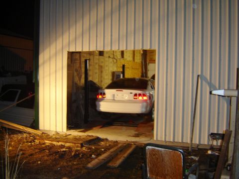 1984 Ford Mustang - A white coupe is positioned on a car lift within a garage structure.
