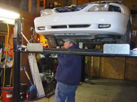 1984 Ford Mustang - A mechanic works on the underside of a white car, which appears to be a 1994 Ford Mustang, elevated on a lift.