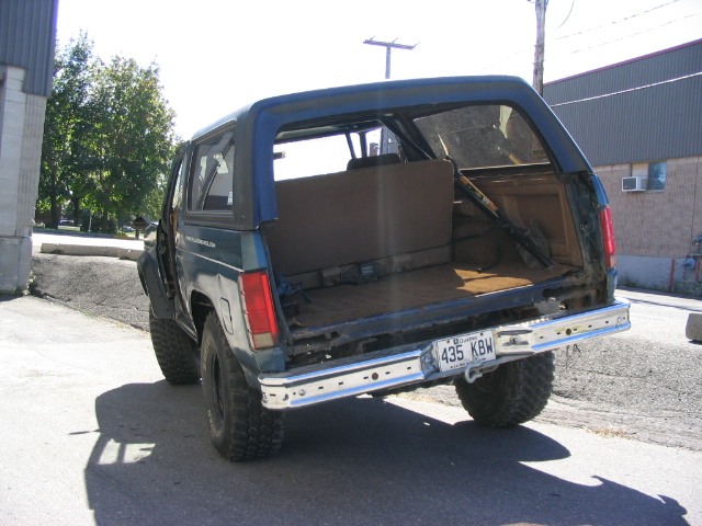 Dark teal Ford Bronco with a blue soft top, rear view, showing a damaged bumper and open cargo area