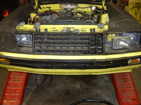 1979 Ford Mustang - Front view of a yellow 1979 Ford Mustang with its hood open, revealing the engine and resting on red ramps.