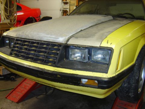 1979 Ford Mustang - Front view of a yellow 1979 Ford Mustang, showing its distinctive grille and scoop hood, in a workshop setting.