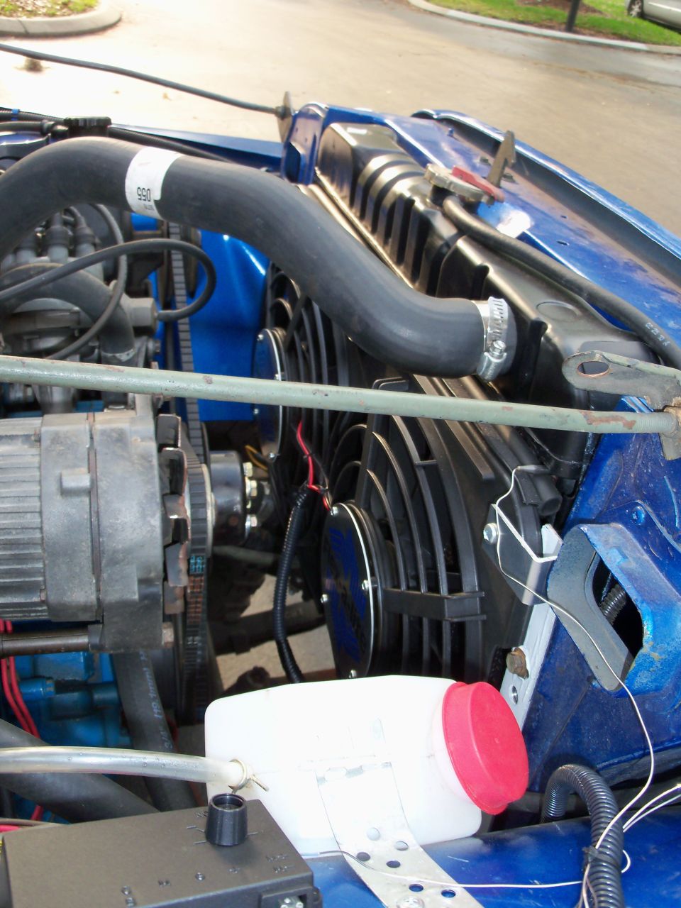 Blue Jeep engine bay with radiator, dual electric fans, alternator, and coolant reservoir