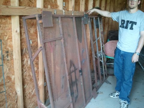 1995 Ford Bronco - A person points to a large, weathered metal roof rack with a perforated design, stored indoors.