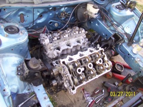1995 Ford Probe - The engine bay of a car is shown with the engine partially removed and disassembled. Tools are visible on the ground.