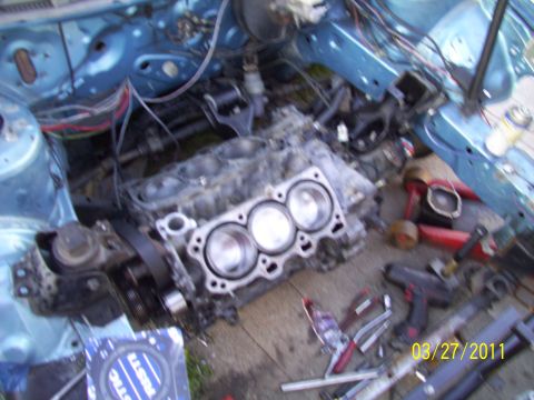 1995 Ford Probe - Disassembled engine and parts are laid out on the ground next to a blue vehicle frame.