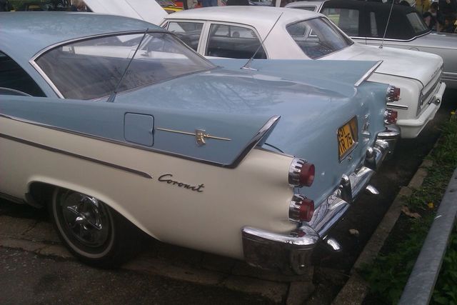 Two-tone blue and white Dodge Coronet with fins and chrome bumper, parked next to other cars