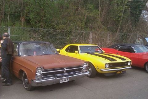 1991 Ford LTD Crown Victoria - A brown 1965 sedan with a black vinyl roof is parked in front of a yellow muscle car.