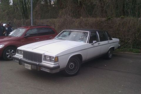 1991 Ford LTD Crown Victoria - A white sedan with a black vinyl roof is parked next to a red SUV.