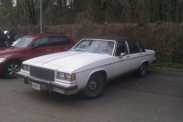 White sedan with black vinyl roof parked next to a red SUV. License plate reads 425 EDV 77