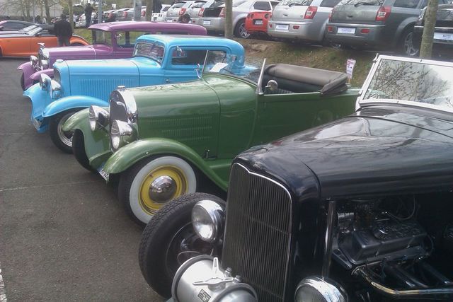 Several classic cars parked in a row, including a green convertible and a blue coupe