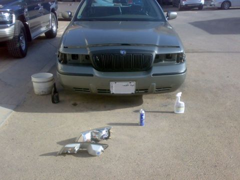 2001 Mercury Grand Marquis - The front of a Mercury Grand Marquis is shown with its headlights removed, and a new pair of headlights are on the ground nearby.