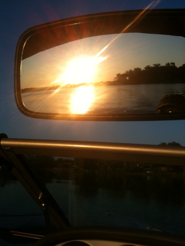 Sunset over the water reflected in a ski boat's rearview mirror above the aluminum windshield frame